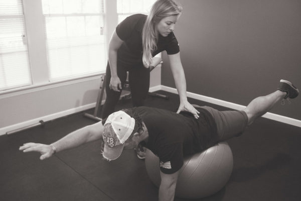 Dr. Meghan Faulkner helping man balance on stomach on workout ball black and white photo